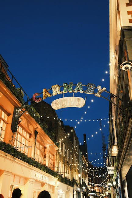 Nighttime view of a busy urban street with multiple vertical neon signs hanging above the sidewalk, displaying words like 'UNITY', 'STRENGTH', 'CREATE', 'PLANET', 'DANCE', 'FAMILY', and 'SOHO'. The si