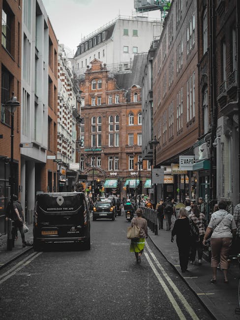 View of a row of shops on a busy urban street in Soho, showing three ground-floor retail stores with signage for Starbucks Coffee, Muncheez, and Amo Amo. The buildings are three stories tall, with the